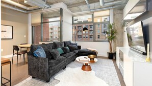 A modern living room with a sectional sofa, a white rug, and a flat-screen TV. - Union Station downtown and gameday retreat! (Denver)