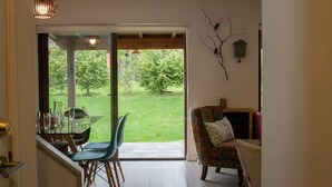 Une pièce dotée d’une porte vitrée donnant sur un jardin, d’une table à manger avec des chaises et d’un canapé avec des coussins.