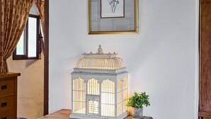 Un farol blanco sobre un aparador de madera, un cuadro en la pared y una ventana con cortinas.