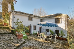 Un bâtiment blanc avec un toit en tuiles, des marches en pierre, du mobilier d’extérieur et des plantes en pot.