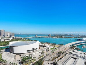 A modern stadium with a large central dome and surrounding seating areas, connected to a marina with boats and a bridge in the background. - Open Studio with Floor-to-Ceiling Bay Views (Miami)