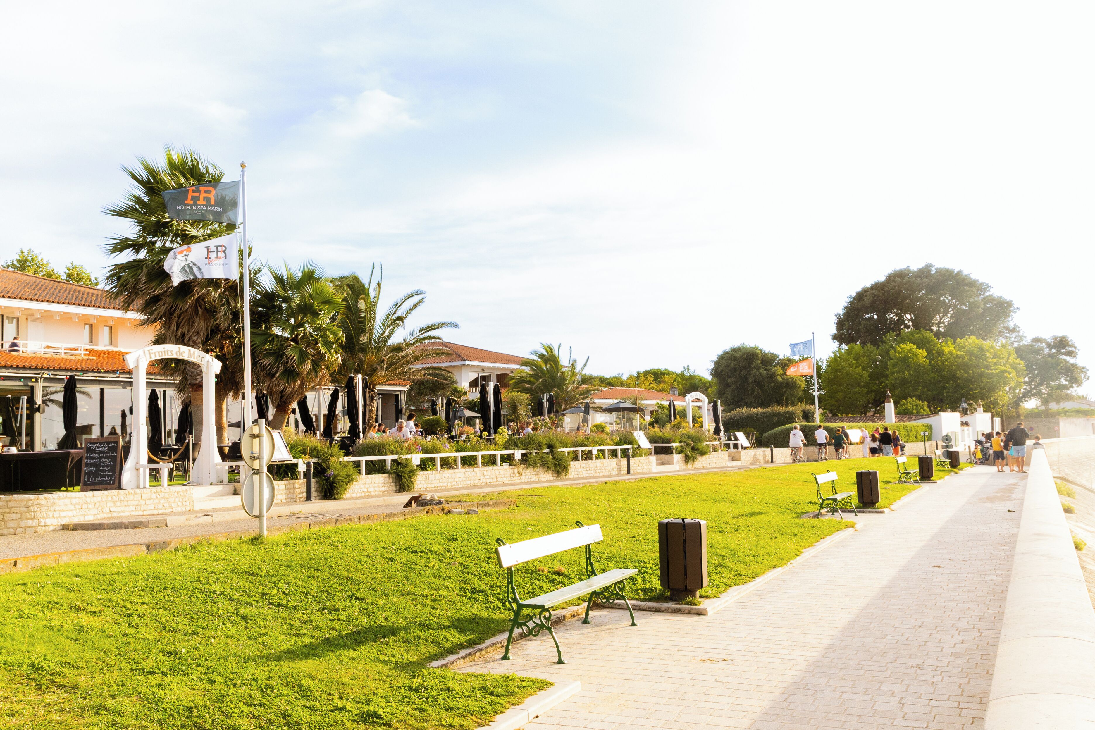 Eine Uferpromenade mit Bänken, einem Mülleimer und einem Restaurant mit Außenbereich.