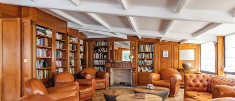 A library with leather chairs, a fireplace, and bookshelves.