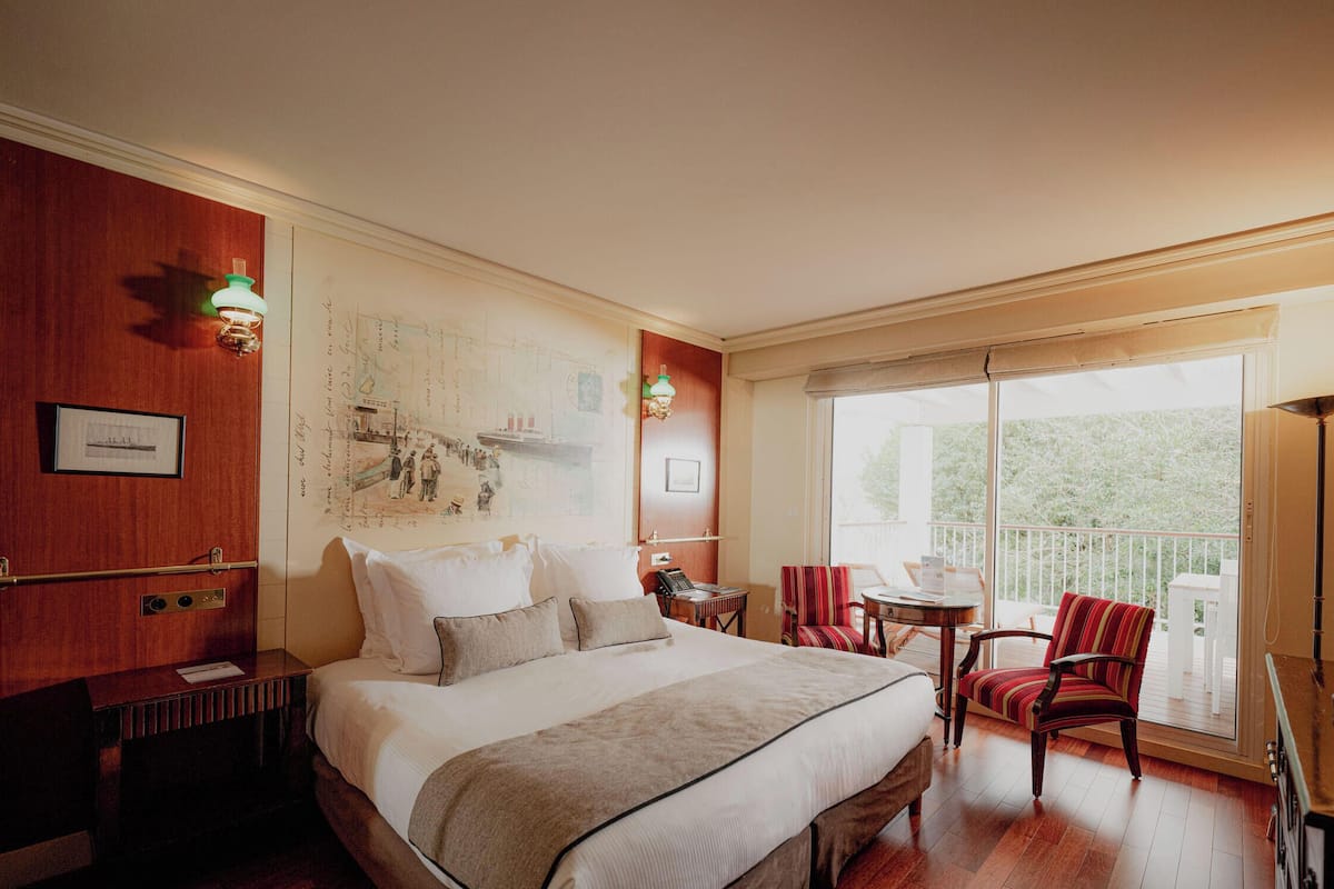 A hotel room with a large bed, a desk, a chair, a balcony with a view, and a map on the wall.