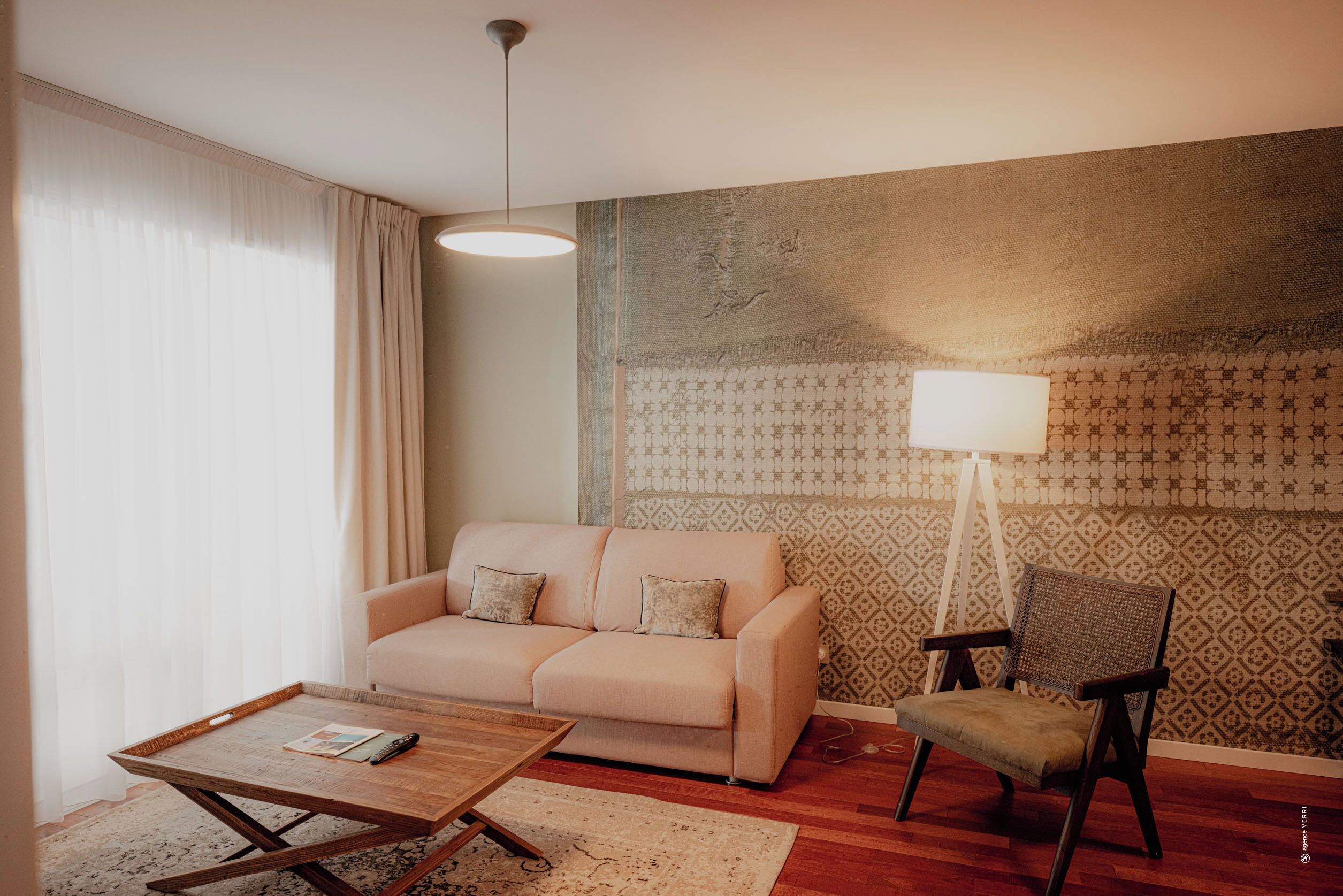 A living room with a sofa, a chair, a coffee table, a lamp, and patterned wallpaper.