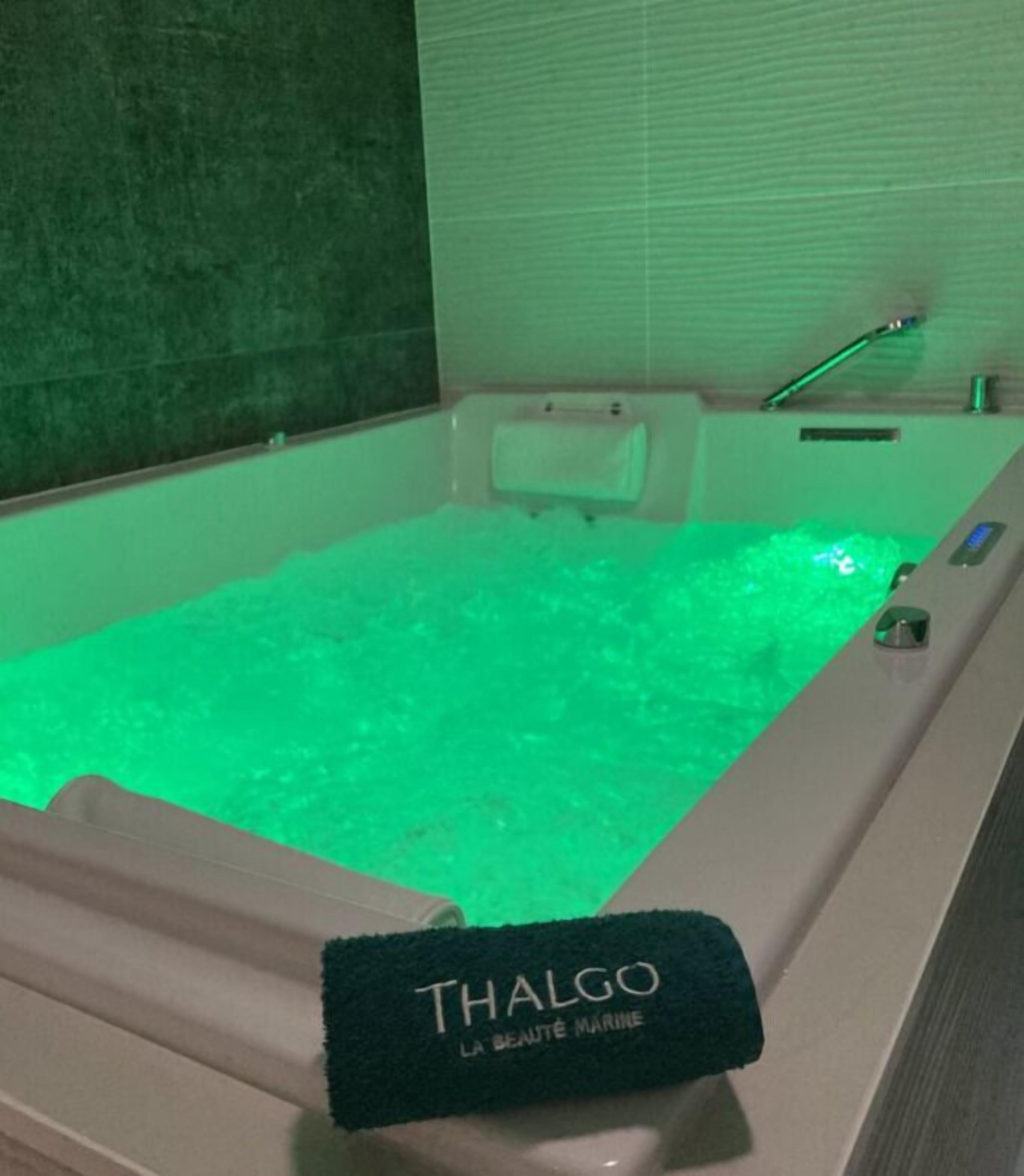A bathtub with a green light, a towel rack, and a sign that reads 'Thalgo Marine.'