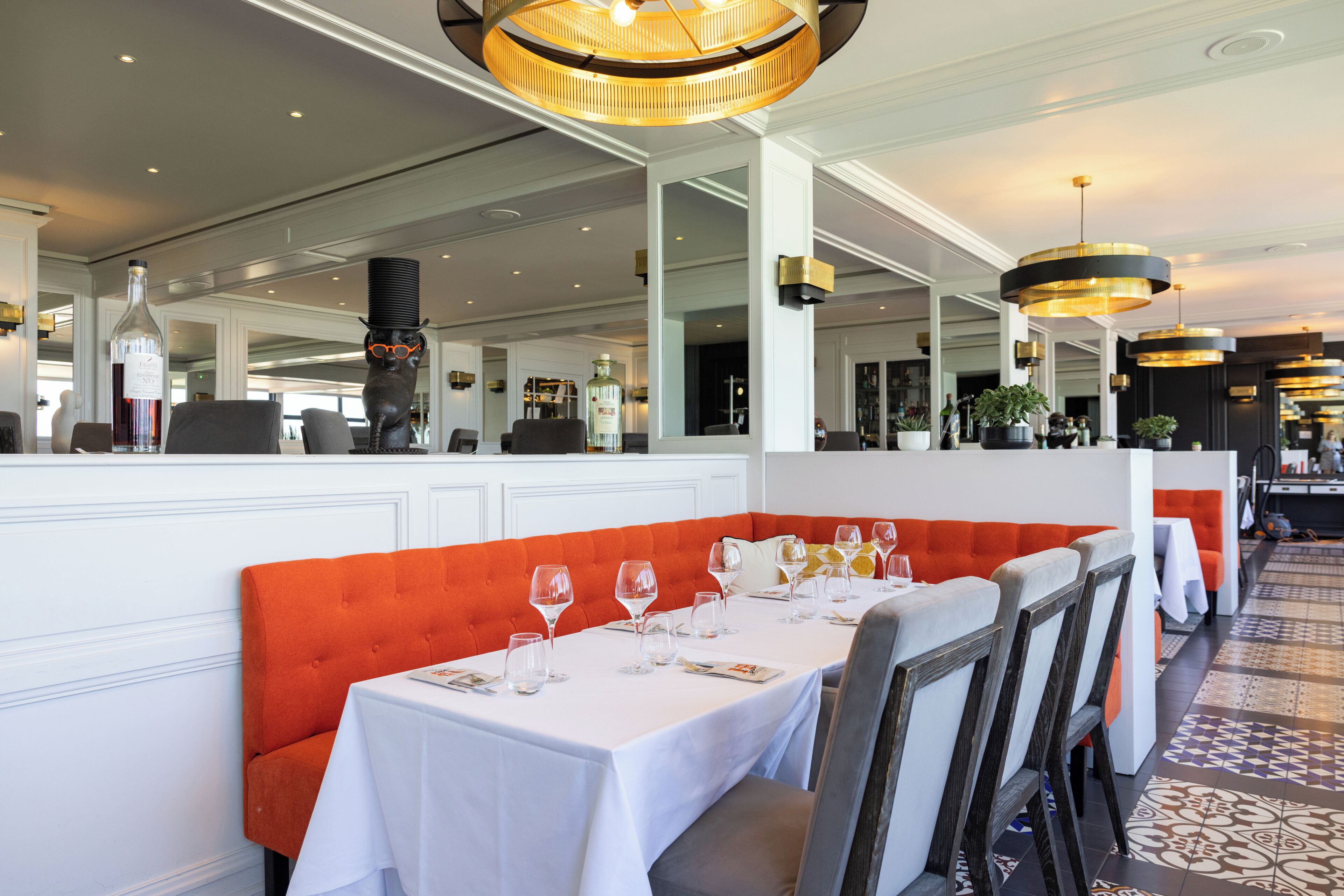 Restaurante com mesas brancas, assentos laranja e iluminação pendente.