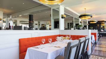 Restaurante com mesas brancas, assentos laranja e iluminação pendente.