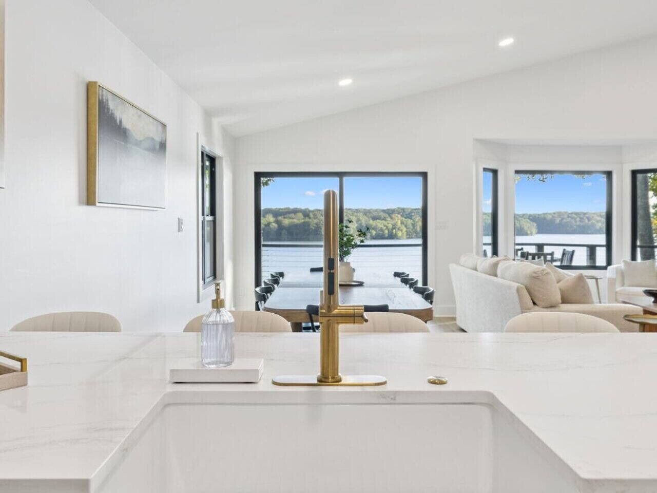 Un salon moderne avec une grande fenêtre donnant sur un lac, un canapé blanc et une table basse en marbre.