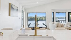 Un salón moderno con un gran ventanal con vistas a un lago, un sofá blanco y una mesa de centro de mármol.