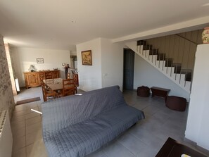 A living room with a sofa, a dining area with a table and chairs, and a staircase. - Holiday Home 'Le Gîte Du Vieux Mûrier Côté Sud' with Private Garden, Wi-Fi and Air Conditioning (Saint-Jean de Serres)