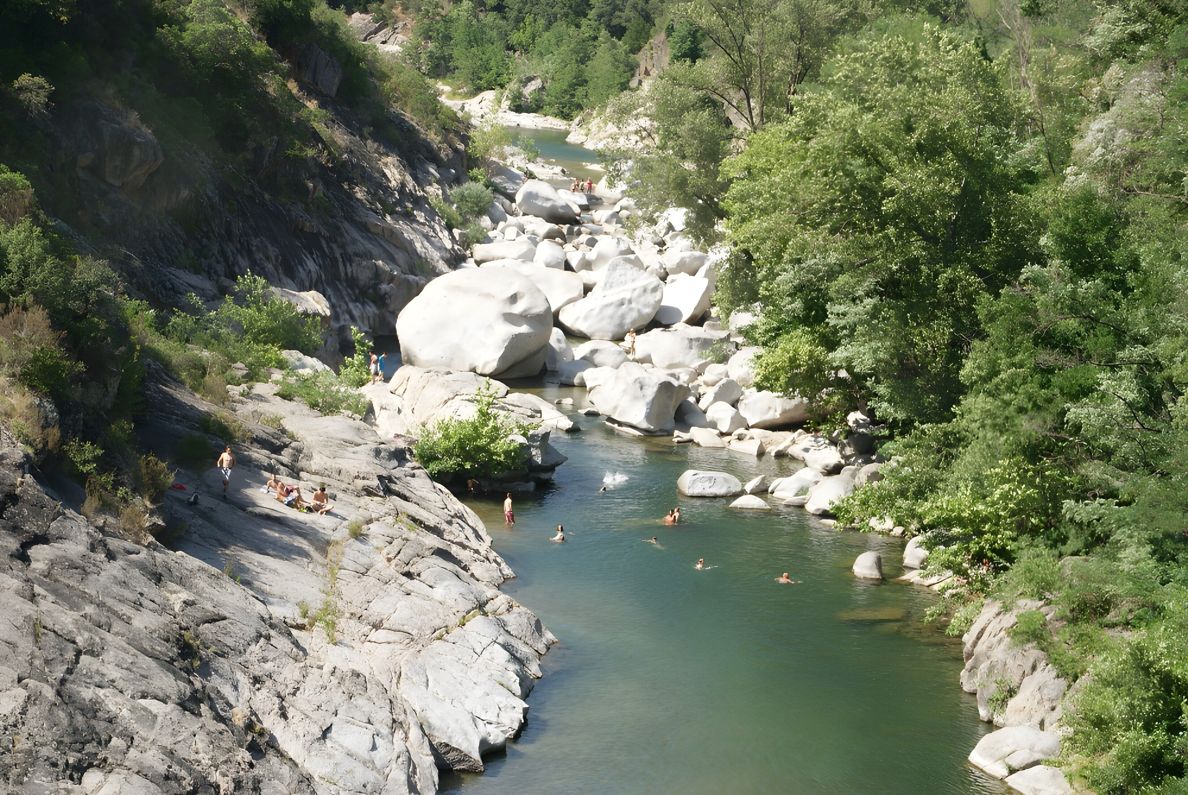 Un fiume circondato da rocce e vegetazione, con persone che nuotano e si rilassano.