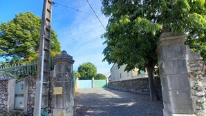 Un cancello con pilastri in pietra, un vialetto sterrato e una recinzione in metallo.