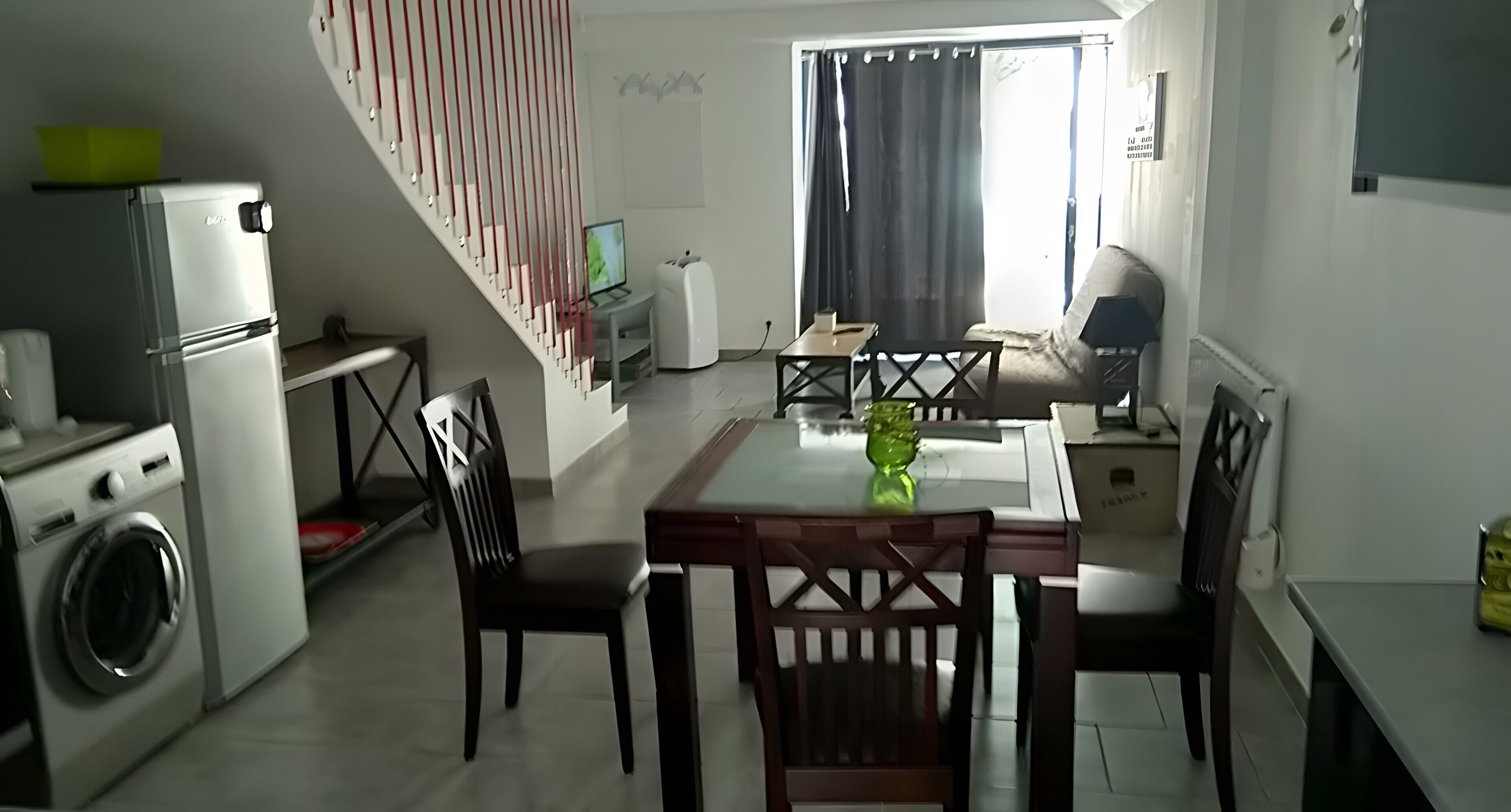 Un espace de vie compact comprenant un coin repas, un lave-linge, un téléviseur et un escalier.