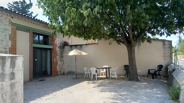 Un patio con tavolo e sedie, un albero e un edificio con un muro in mattoni e una porta.