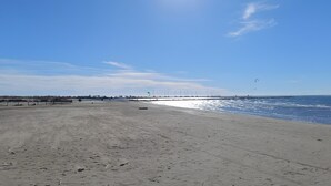 A beach with a sandy shore, a wooden fence, and sailboats in the distance. - “Sea & Sun” Apartment with Private Terrace (Port Camargue)