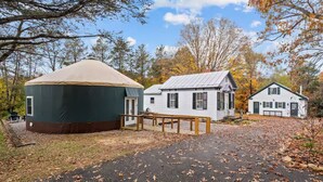 A yurt, a white house, and a white cabin in a forested area with autumn leaves. - Shenandoah Valley Cottage (Stanley)