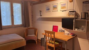 Huoneessa on sänky, työpöytä, tuoli, televisio ja patteri.