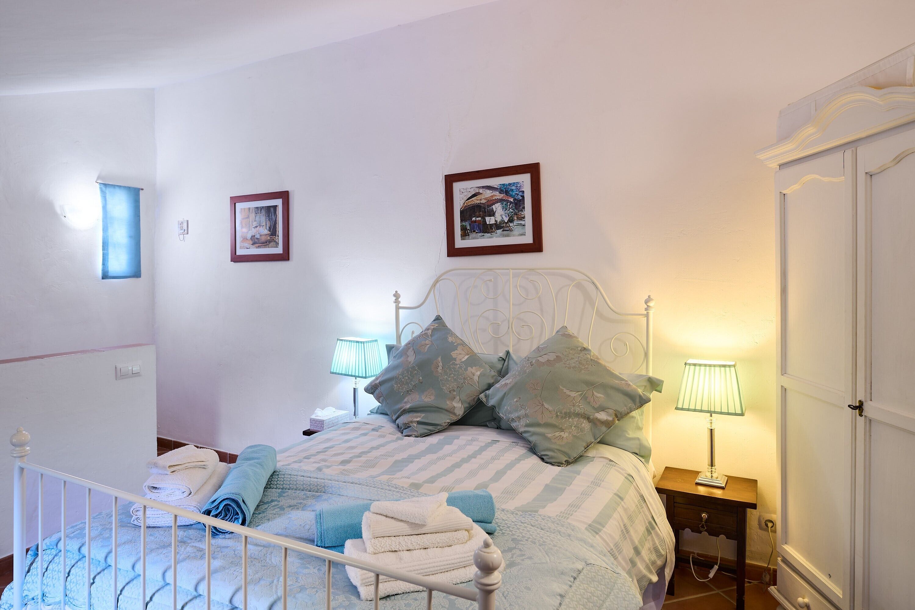 A neatly made bed with pillows, a bedside table with a lamp, and two framed pictures on the wall.