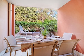 Zona pranzo con tavolo imbandito per quattro persone, sedie e vista su un giardino con alberi e un patio.