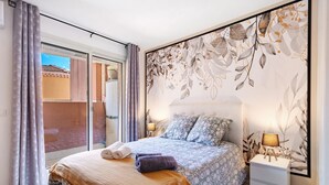 Ein Schlafzimmer mit einem Bett, einem Nachttisch, einer Lampe und einem großen Fenster mit Vorhängen.