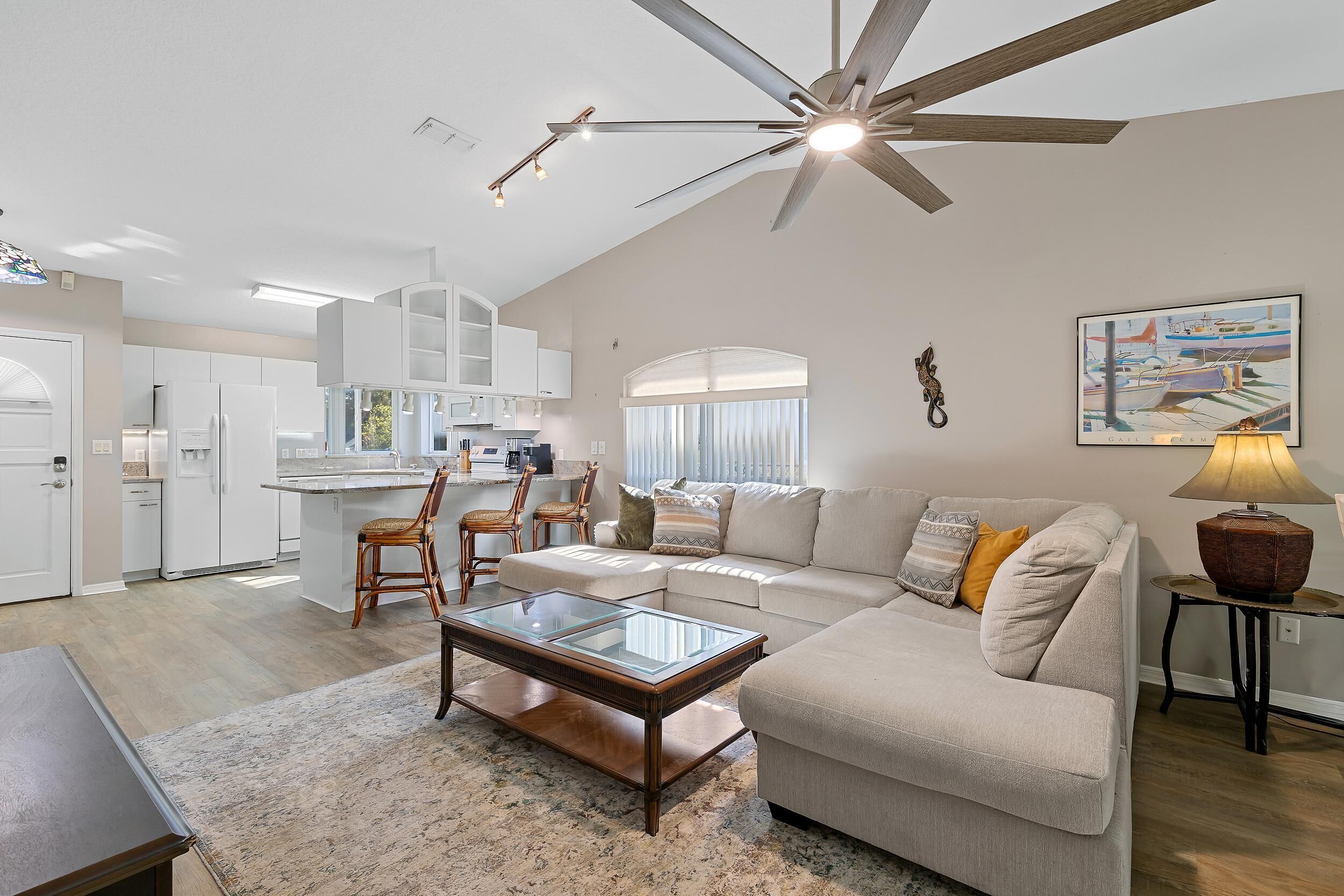 A spacious living area with a high ceiling fan, a glass coffee table, a sofa, and a dining area with chairs.
