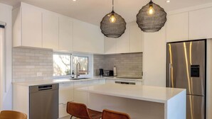 A modern kitchen with white cabinetry, a stainless steel dishwasher, a large island with bar stools, and a built-in oven.
