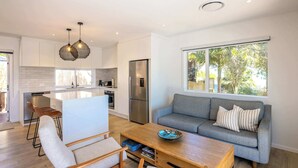 A modern kitchen with white cabinets, a stainless steel refrigerator, and a dining area with a wooden table and chairs.