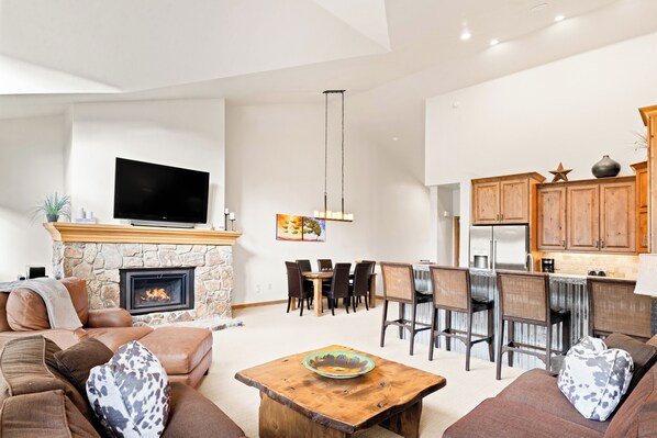 A spacious living room with a fireplace, a flat-screen TV, and a dining area with a kitchen in the background. - Private Hot Tub & Garage, Near Main St/Peak 9 (Breckenridge)