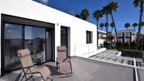 A modern outdoor patio with two lounge chairs and a glass door leading to a covered area. - Villa Levante, Modern Costa Blanca villa with pool and sunny terrace (San Fulgencio)