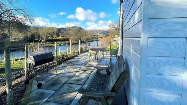 Eine Terrasse mit Grill, Sitzgelegenheiten im Freien und Blick auf einen See und Hügel.