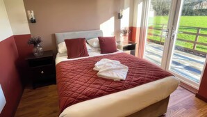 Ein Schlafzimmer mit einem großen Bett, einem Nachttisch, einer Kommode und einem Fenster mit Blick auf eine grüne Wiese.