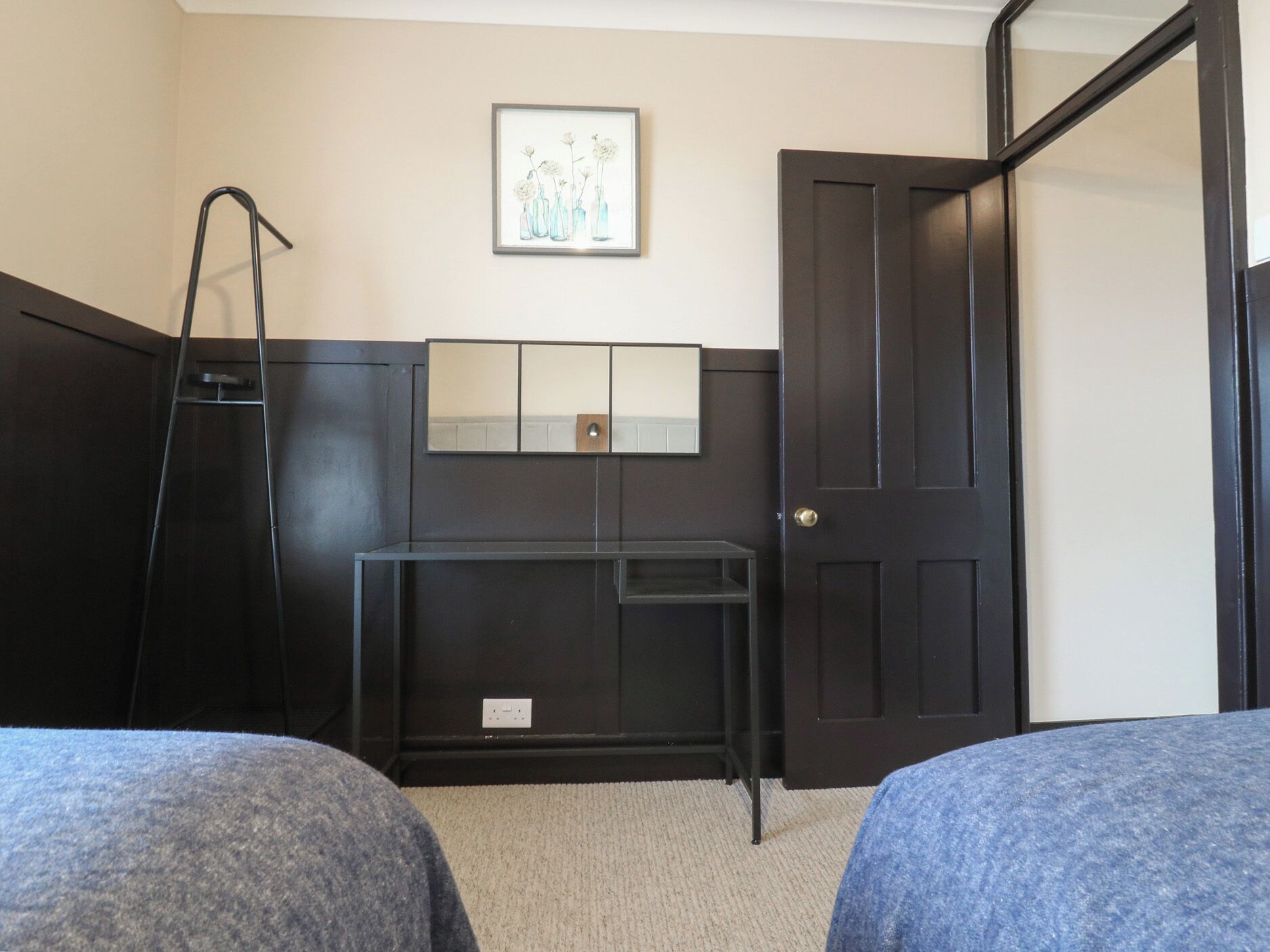 A bedroom with two beds, a desk, a ladder, a door, and a framed picture on the wall.