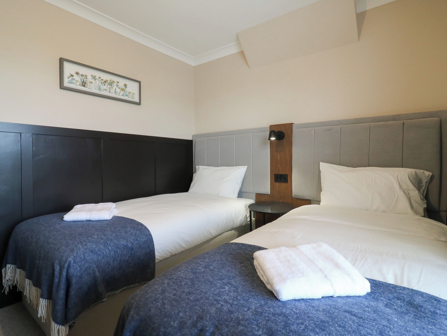 A hotel room with two beds, a nightstand, a lamp, and a framed picture on the wall.