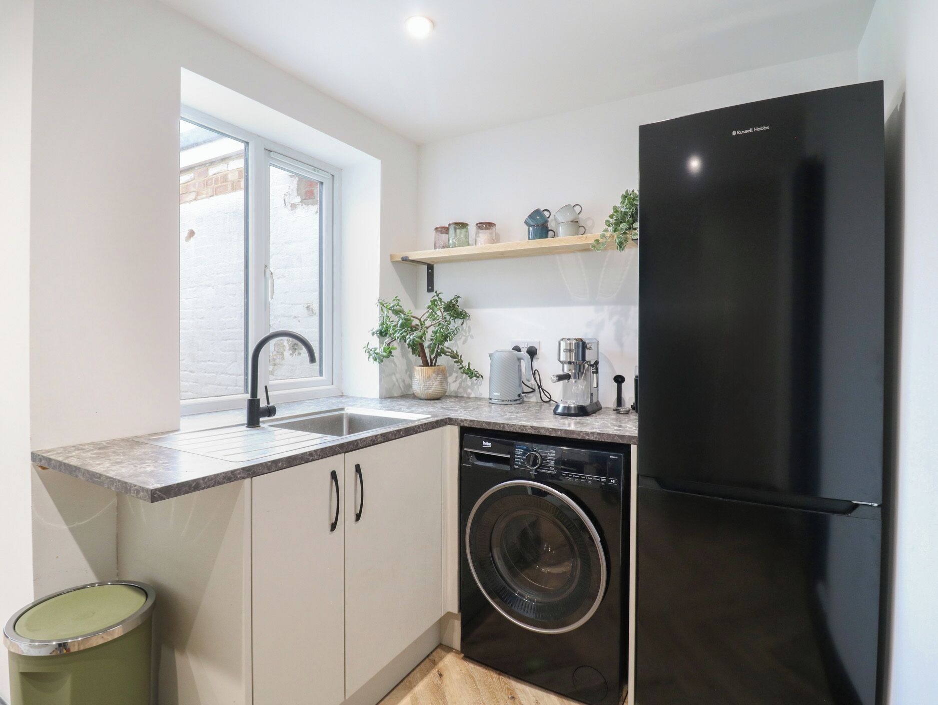 A compact kitchen with a built-in washing machine, a black refrigerator, a sink with a modern faucet, and a window providing natural light.
