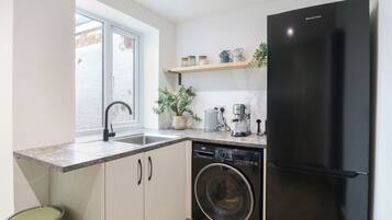 A compact kitchen with a built-in washing machine, a black refrigerator, a sink with a modern faucet, and a window providing natural light.
