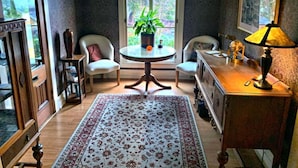 Una habitación acogedora con una mesa redonda, dos sillas, una planta en maceta, una lámpara y un ventanal con vistas al verdor.