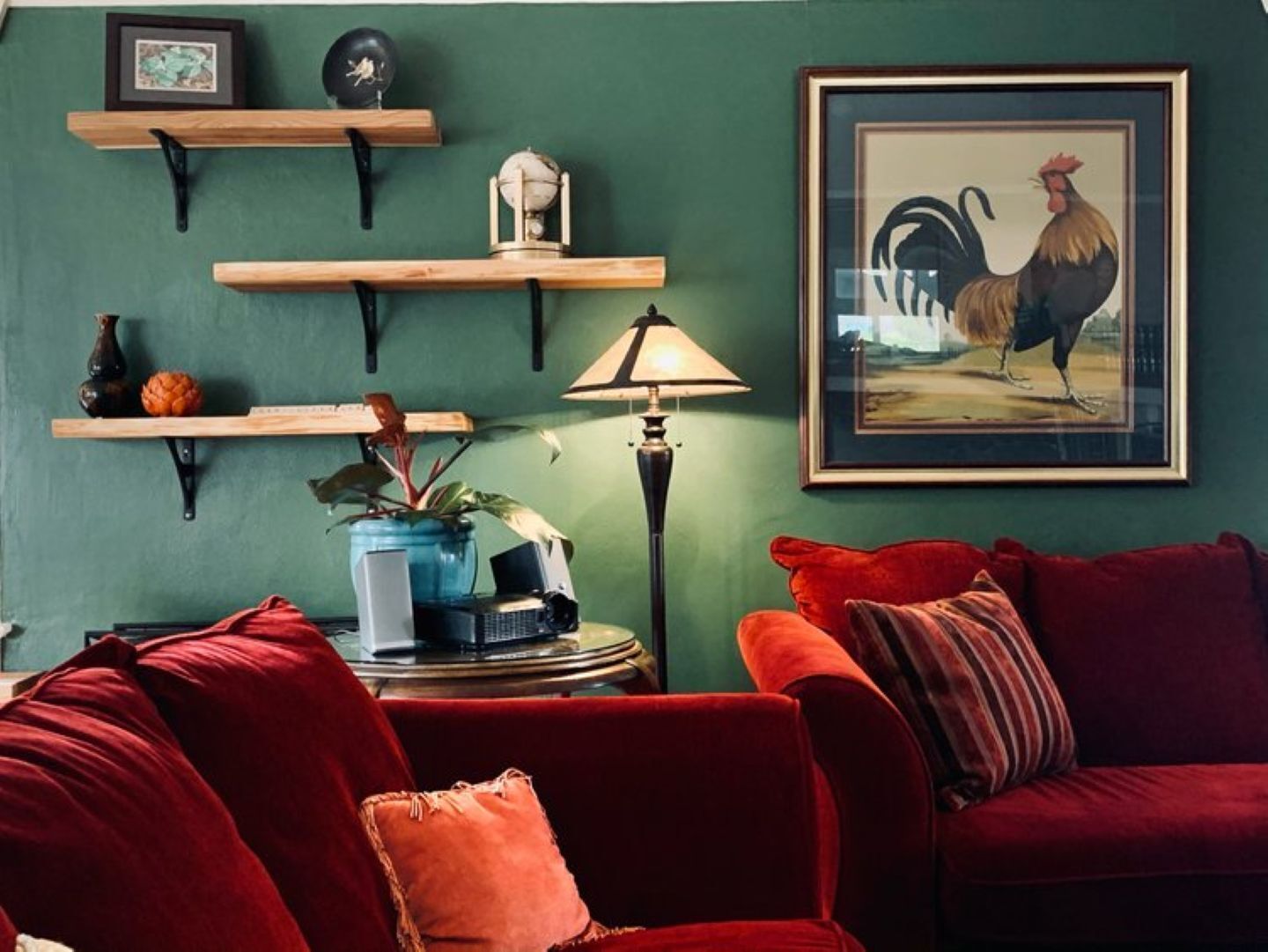 A living room with a red sofa, a lamp, and a framed rooster picture on the wall.