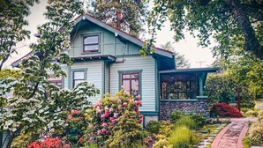 Une maison à deux étages, avec des fondations en pierre et un jardin où poussent différentes plantes et fleurs.