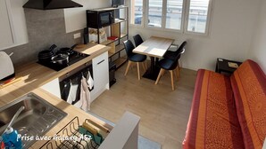 A compact kitchen with a microwave, stove, and sink. There is a dining area with a table and chairs. A sofa is visible in the corner. - WEEKLY rental from SATURDAY to SATURDAY facing the sea QUEND PLAGE LES PINS 80 (quend plage les pins)