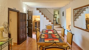 Un comedor con una mesa dispuesta para cuatro personas, una escalera y un ventilador a la izquierda.