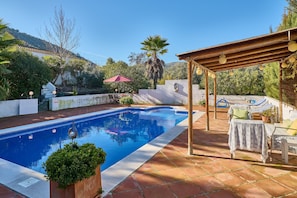 Piscina con una pérgola, mobiliario de exterior y vistas a las colinas.