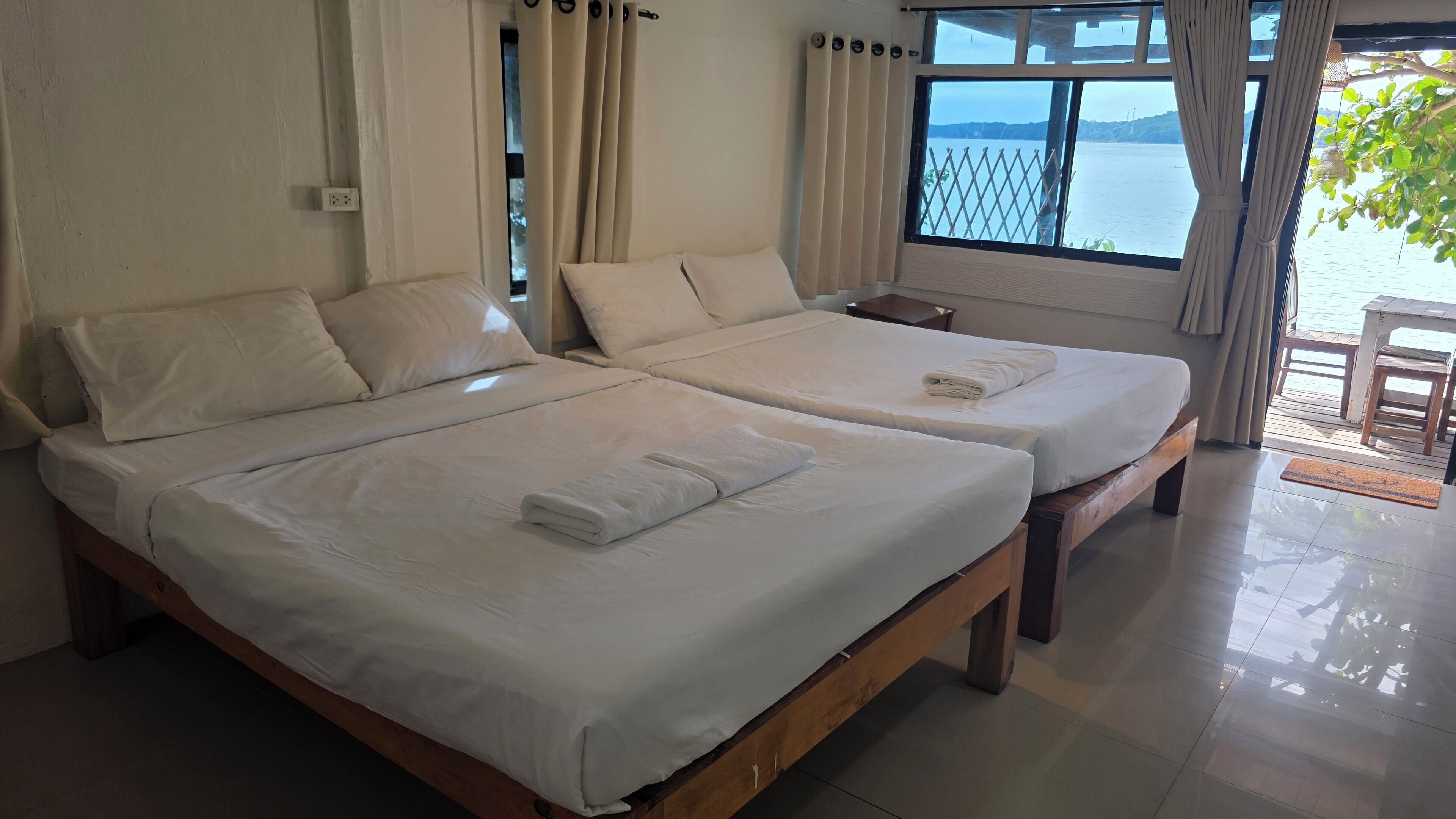 A hotel room with two beds, a window with a view of the sea, and a wooden floor.