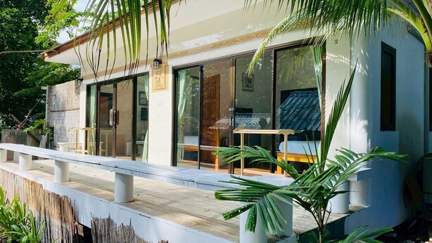 A modern building with large glass windows, a wooden deck, and a bench. - Samed Big Cape Resort (Rayong)