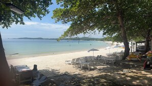 A beach with white lounge chairs and umbrellas, a clear view of the sea, and a distant mountain range. - Samed Big Cape Resort (Rayong)