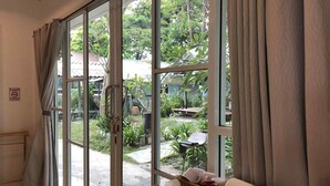 A room with large sliding glass doors leading to a garden, a wooden bench, and a wicker basket with items on a table. - Samed Big Cape Resort (Rayong)