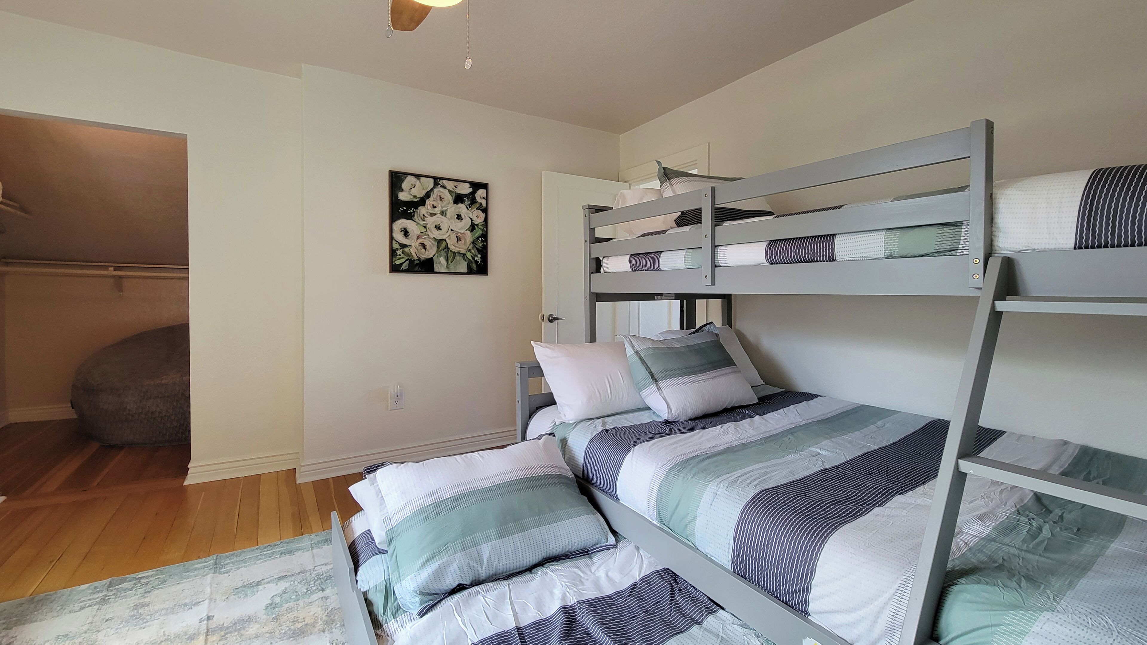 Un dormitorio con una cama litera, un sofá gris, un cuadro de flores y suelo de madera.