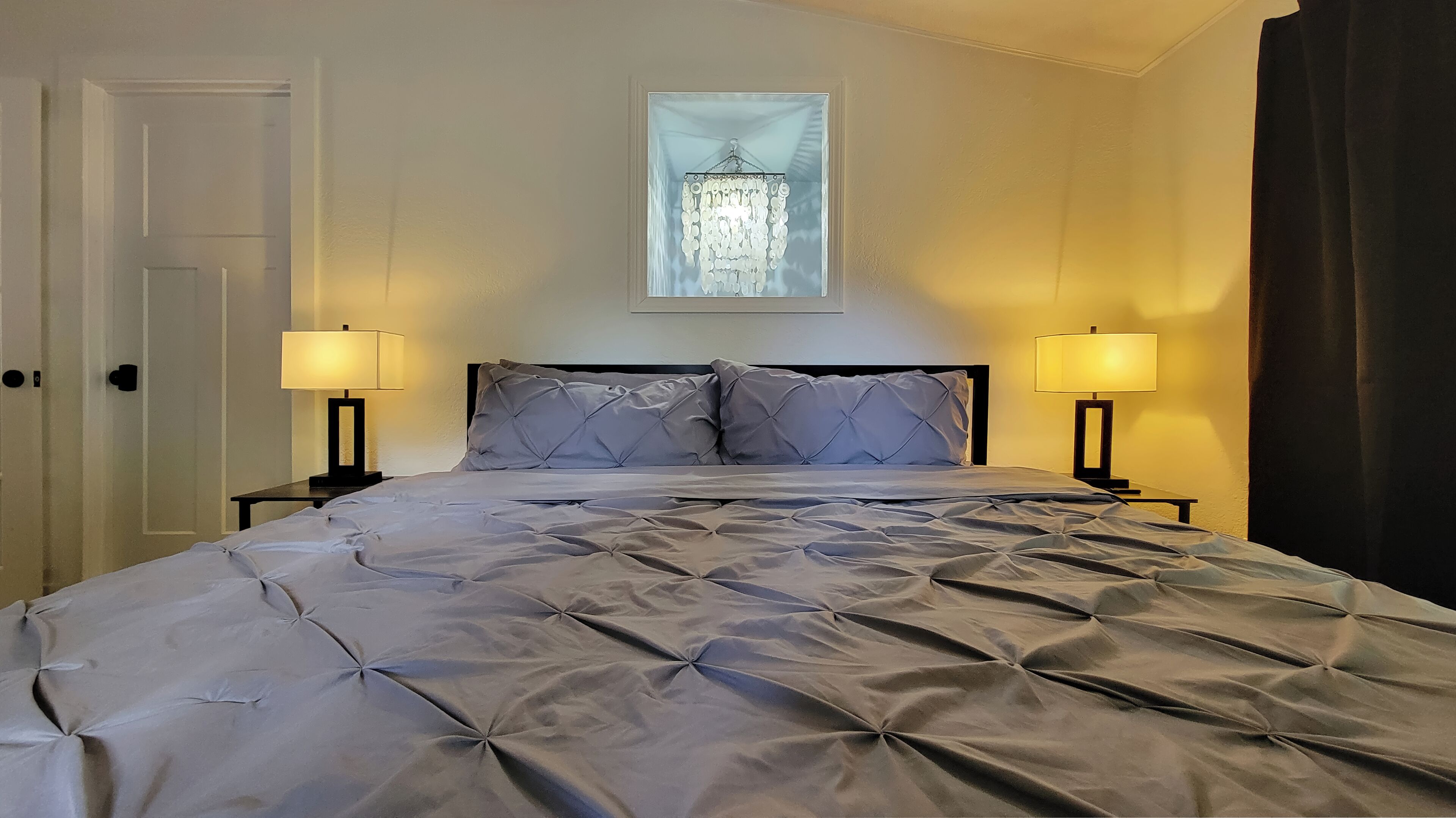 Un lit bien fait, avec une couette matelassée, deux lampes de chevet et un lustre au-dessus.