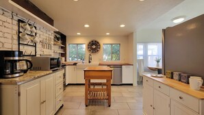 A modern kitchen with white cabinets, a wooden table, and a large clock on the wall. - Rosewood Landing- Hot Tub- Sauna  (Medford)