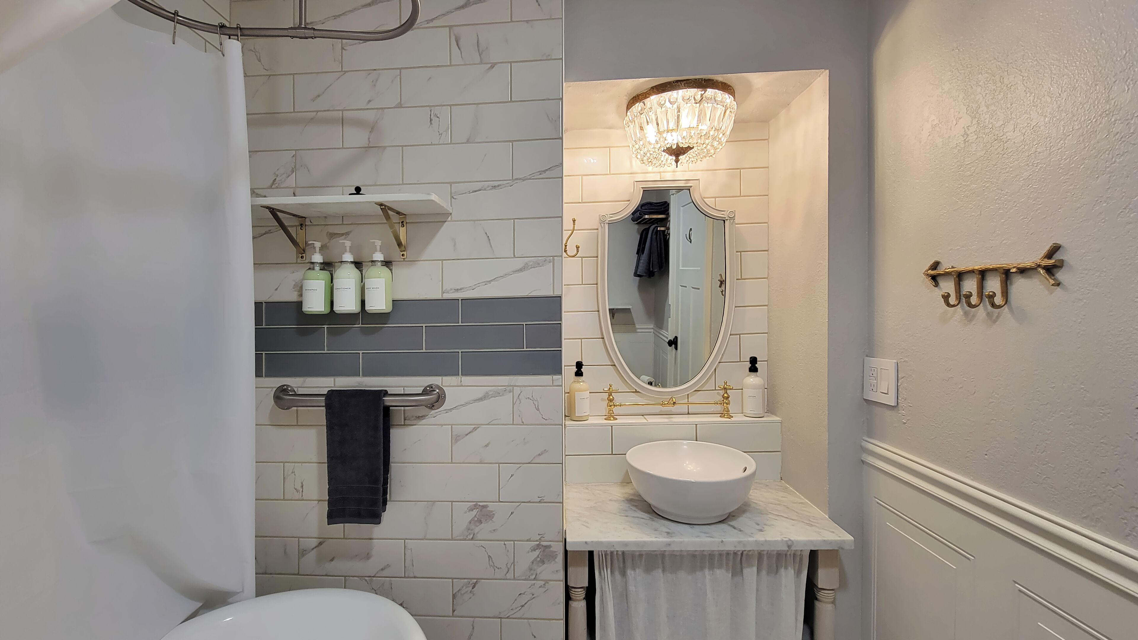 A bathroom with a white toilet, a sink with a marble countertop, a mirror with a gold frame, and a chandelier above the mirror.